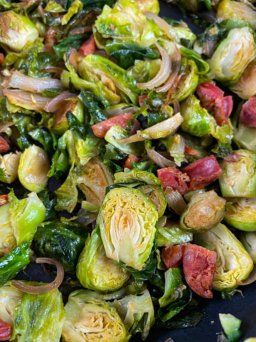 Stock photo showing close-up, elevated view of Brussel sprout halves cooked by stir frying in non-stick frying pan with chopped bacon and chorizo sausage.
