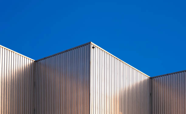 wellblechwand von industriefabrikgebäuden vor blauem, klarem himmelshintergrund mit lichtreflexion auf der oberfläche - architecture roof aluminum sheet industry stock-fotos und bilder