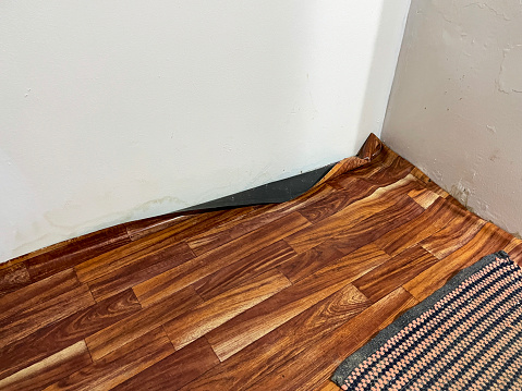 Stock photo showing some vinyl flooring in the corner of a room, which has a realistic laminate wood flooring appearance but has been poorly fitted resulting in crumpled raised effect.