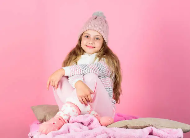 Photo of Keep warm and comfortable. Warm accessories that will keep you cozy this winter. Kid girl wear knitted hat relaxing pink background. Child long hair warm woolen hat enjoy warm. Warm clothes concept