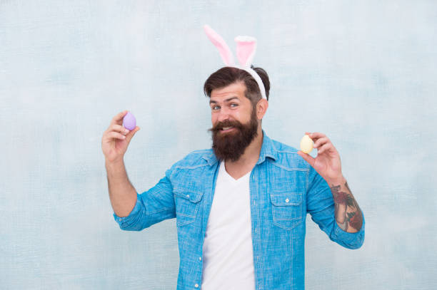 Celebration of spring holiday. Bearded man bunny ears and Easter eggs. Everything you need for Easter is here. Hipster long ears holding egg. Culture customs and traditions. Easter bunny colored eggs.
