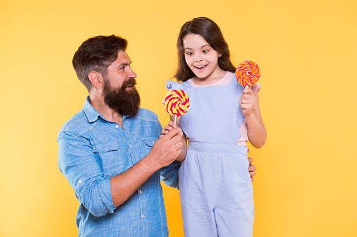 Taste the rainbow. Family of father and daughter eat candies. Happy family yellow background. Bearded man entertain little child with treats. Family time. Love and trust. Fun thing family do together.