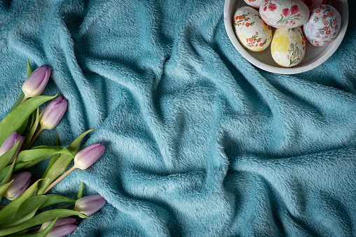 Painted Easter eggs in a bowl and gorgeous bouquet tulips on a romantic soft and cosy blue blanket copy space