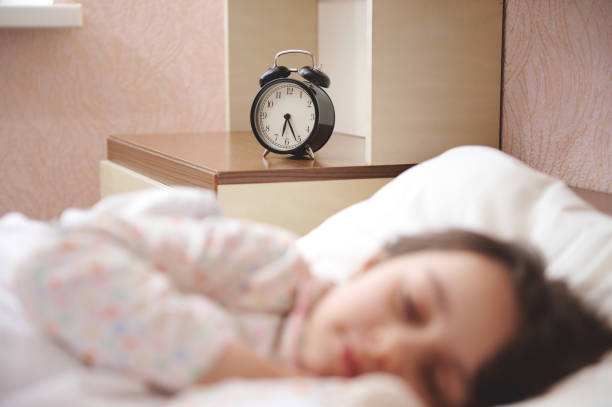 istock Focus on black alarm clock showing half past six, on bedside nightstand, in blurred foreground of a sleeping child girl 1474199686