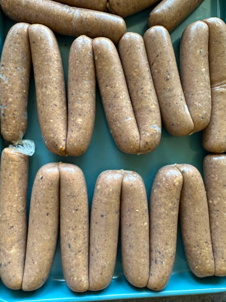 image plein cadre d’un chapelet de saucisses maison, rangées de saucisses de porc non cuites sur un plateau de four en métal bleu, vue surélevée - four objects apple fruit color image photos et images de collection