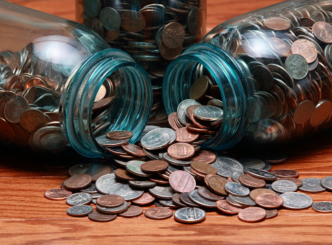 Coins spilling out of a blue canning jar on a wood surface