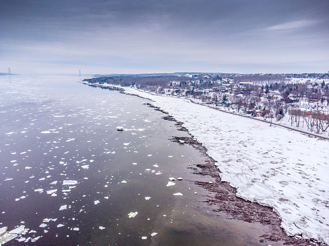 Aerial view of St-Lawrence river coast during winter day. Ice is floating on the water.