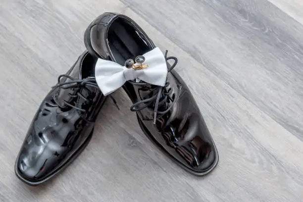 A display of the groom's black wedding shoes, white bowtie and his black and silver cufflinks.