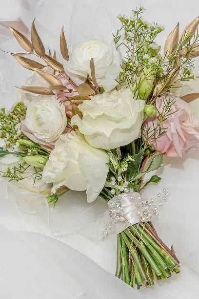 A gorgeous soft ivory and pink pastel colored bridal bouquet against the wedding dress.