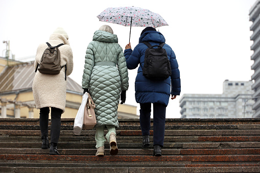 Moscow, Russia - March 2023: Three women with one umbrella walking up the steps on city street