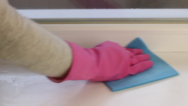 Womans hands with rubber gloves cleans the windowsill close up. Window washer.