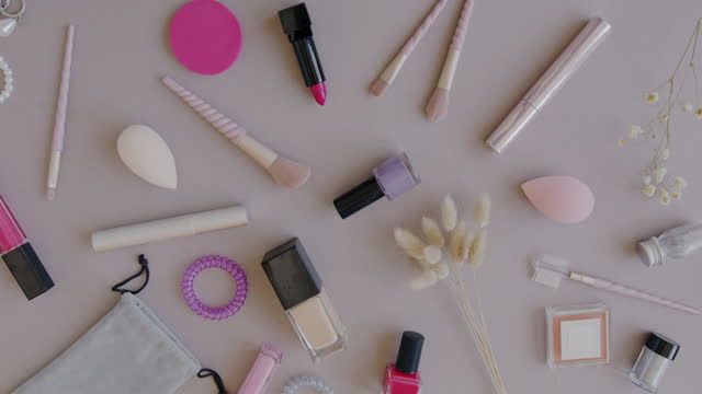 Close-up of diverse female accessories and make-up products and female hand putting flower designing flat lay