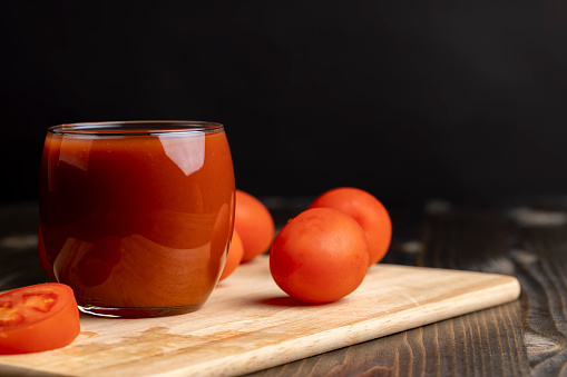 Fresh red tomato juice poured into a glass, fresh tomatoes and juice on a wooden table