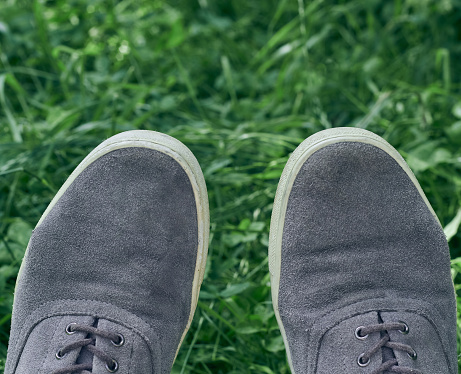 Young man in gray sneakers on green grass in field. Gray sneakers on green grass