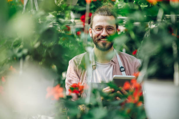 istock Man gardener working in a greenhouse and using a tablet 1474224264