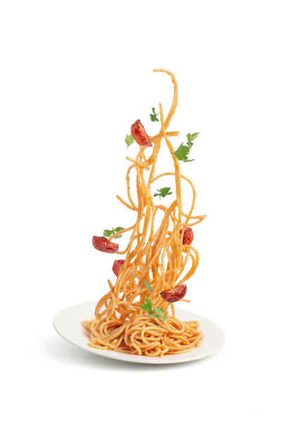 Pasta with tomatoes and basil falling into a plate, levitation.White saucepan with pasta and vegetables, tomatoes and herbs flying in the air on a white isolated background. Levitation.