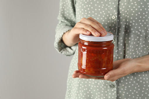 Woman holding jar of canned lecho on light background, closeup. Space for text