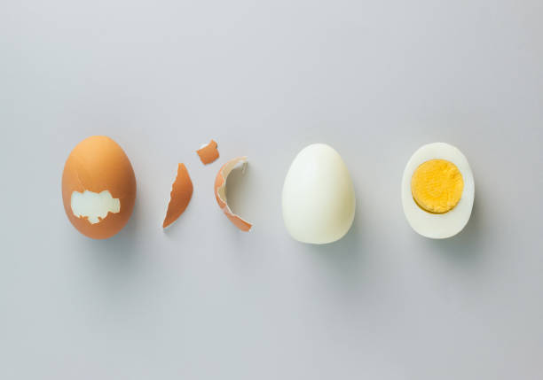 istock Whole chicken egg, egg without eggshell and cracked half in the middle with yolk on grey background. Minimal healthy food concept. Top view, flat lay. 1474228688