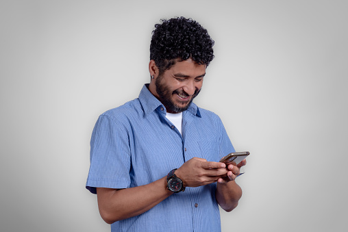 Portrait of young man from the side sending message on cell phone in studio with gray background. High quality studio shots.