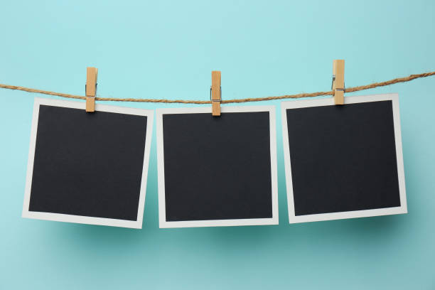 istock Wooden clothespins with empty instant frames on twine against light blue background. Space for text 1474231297