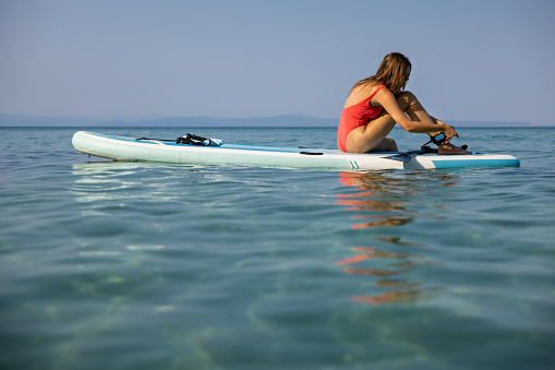 Young Caucasian woman in pink swimwear, enjoying the vacation while exploring sea with standup paddle board
