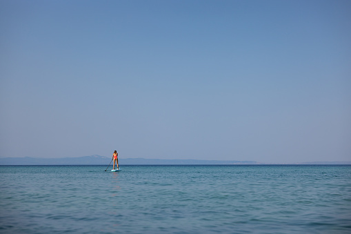Young Caucasian woman in pink swimwear, enjoying the vacation while exploring sea with standup paddle board