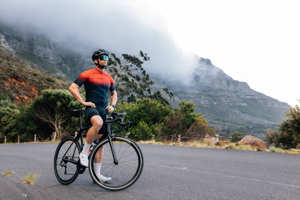 istock Young male cyclist relaxing after training with hands on a hips. Professional athlete with road bike enjoying the view while standing on a road in wild terrain. 1474236896