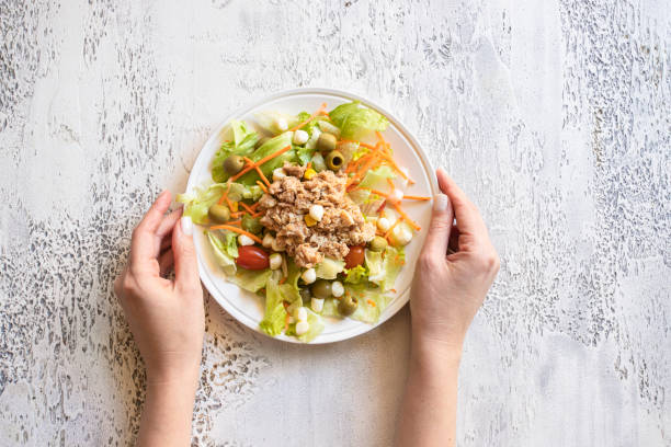 istock Hand holding classic tuna salad with  different lettuce on white concrete backgroind.Top view 1474240504