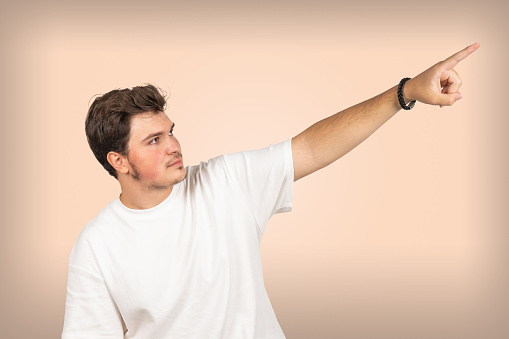 Young man pointing to the sky with his index finger. The man is wearing a white T-shirt. Studio photo taken on isolated background.