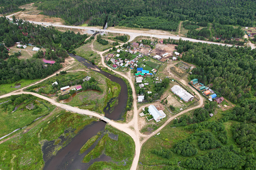 Aerial view of the village among the coniferous forest. Countryside in summer. Village houses, river, roads.