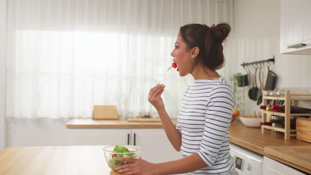 Caucasian young woman eating healthy green salad in kitchen at home. Attractive beautiful vegetarian woman feel happy and enjoy healthy foods for breakfast to lose weight and health care in house.