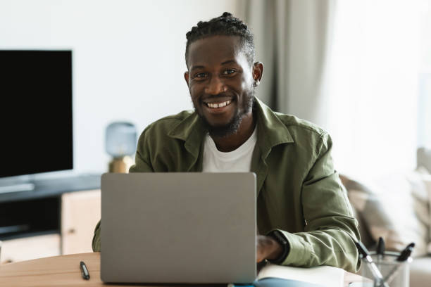 istock Cheerful african american guy programmer sitting at workdesk at home, male freelancer sitting in front of computer 1474251126