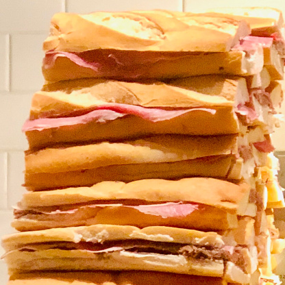 A freshly made stack of Cuban sandwiches - split Cuban bread layered with split bread in half then layer the sandwich with mustard, cheese, pickles, ham, and pork - sit ready to serve at a restaurant in Hoboken, New Jersey.