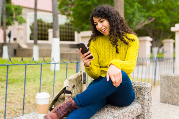 istock Excited woman smiling while texting on her phone in the park 1474262390