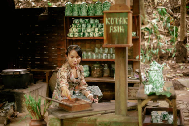 Asian Girl in Kebaya Using Stone Mortar Making Herbal Tea in Old Style Javanese Public Kitchen stock photo