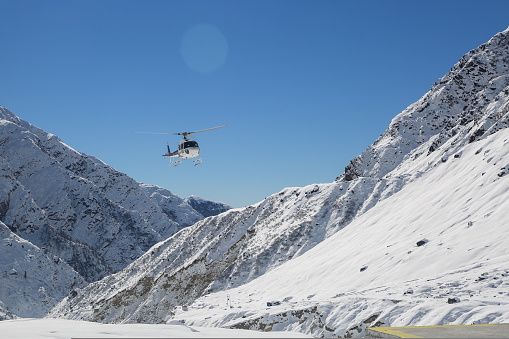 Helicopter flying in snow covered valley of Mountain in Himalaya. White helicopter on a white landscape with clear blue sky background.
