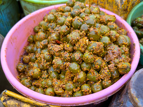 Stock photo of bucket filled with hot tenti / kerda berry pickle at Indian market, spicy street food for sale at outdoor chutney stall / stand, elevated view of fermented condiment in India