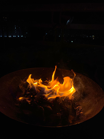 Stock photo displaying a fire pit with coals and wood that has been set alight during a dark period of the night. The glow of the fire and charcoal is lighting up the surroundings slightly.