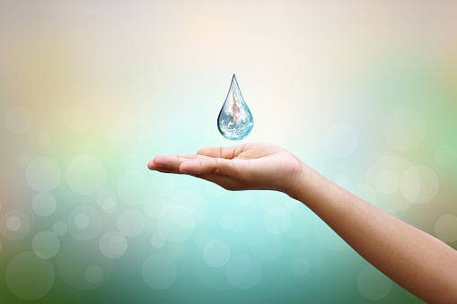 World Water Day Hands waiting for the world in water drop shape on background blurred flowers and sky with the light of the sun. Elements of this image furnished by NASA.