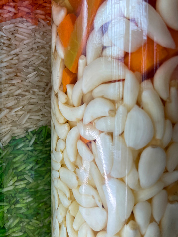 Stock photo showing a close up a glass bottle, full of garlic and chilli pepper oil being marinaded, it is next to another bottle full of rice in the colour of the Indian flag, green, white and orange