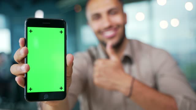 Close up of smartphone with green screen showing young businessman sitting in modern office. Color key, vertical template layout for advertising.