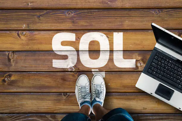 Photo of Legs in sneakers standing next to laptop and SQL on wooden floor.