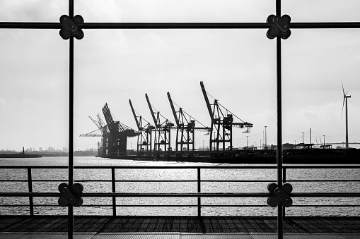 View through a large modern glass window, the silhouettes of harbor cranes and industrial buildings to be seen in the background, horizontal