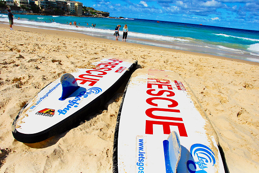 North Bondi Beach, New South Wales, Australia - April 8, 2007: Two “SURF RESCUE” surfboards used by the North Bondi Surf Life Saving Club lies on North Bondi Beach awaiting use in an emergency as swimmers and surfers enjoy the beach in the distance.