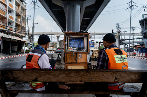 Motorcycle taxi drivers watch a Muay Thai fight on a DIY satellite TV setup at their taxi stand situated beneath an underpass in East Bangkok.