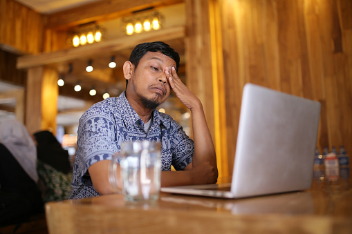 Asian man having eye pain while working in cafe