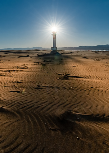 maritime lighthouse with the Sun behind illuminating the lighthouse during a sunset in the Ebro Delta, Spain. Vertical photography with copy space.