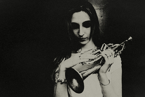 A young woman with a trumpet looks down thoughtfully.