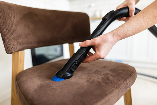 Close-up view of vacuuming the chair using an upholstery brush