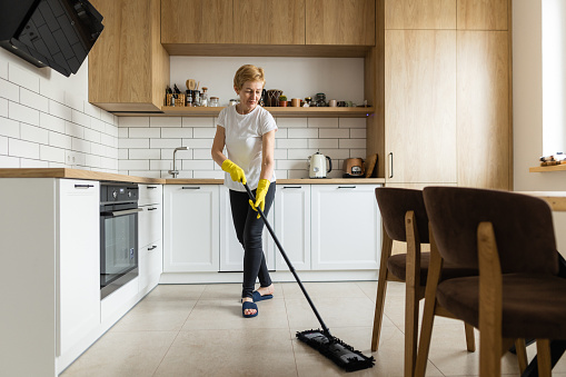 The mature housewife using the chenille mop to clean the floor in the kitchen at home